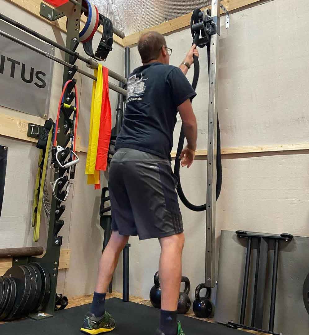 RopeFlex RX505 Hydra Friction Rope Training Drum - A man in an indoor facility is pulling a rope from a hanging gym equipment