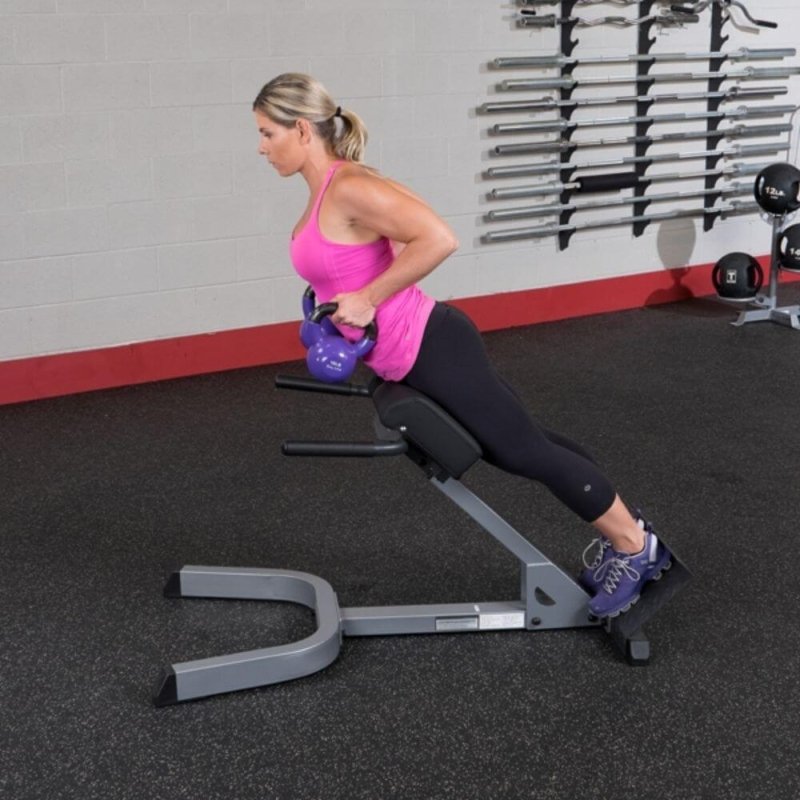 Body-Solid 45° Back Hyperextension GHYP345 - Woman in pink top using GHYP345 while holding 2 purple kettlebells