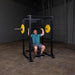 Body-Solid GPR400 Power Rack - Man sitting and holding the barbell up with one plates on opposite side in color yellow 