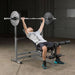 Body-Solid PowerCenter Rack Bench Combo GDIB46L - Man working out pull up a barbell while laying down on a bench