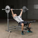 Body-Solid PowerCenter Rack Bench Combo GDIB46L - Man working out pull up a barbell while laying down on a bench