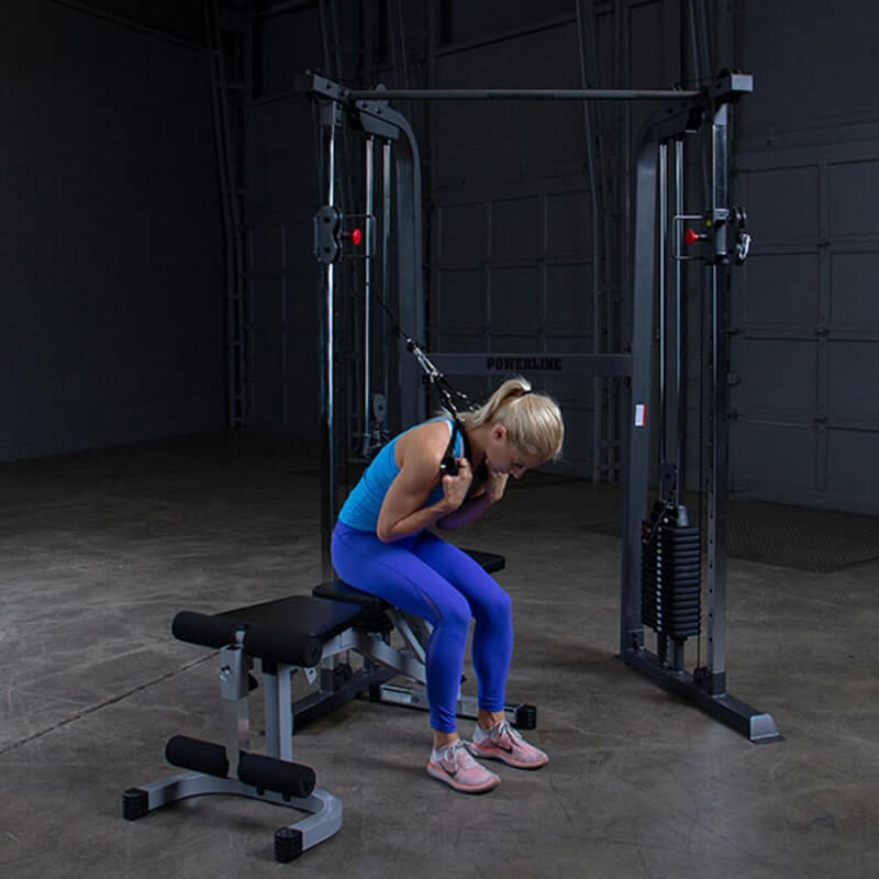 Body-Solid Powerline PFT100 Functional Trainer - metal bar with a bench in a room