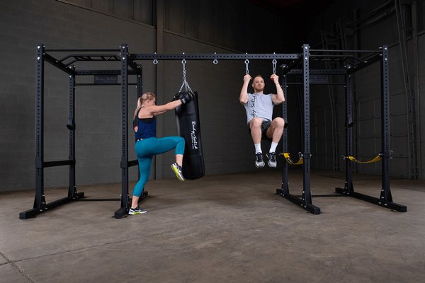 Body Solid Pro Club Line Power Rack, Half Rack Connecting Bar - man doing pull ups and woman kicking the bag 