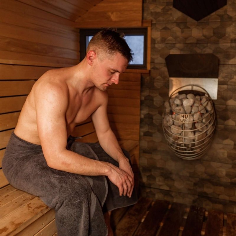 HUUM DROP 9 kW 240V Electric Sauna Heater - a man sitting next to a metal basket 