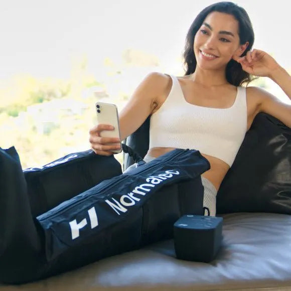 Hyperice Normatec 3 Leg Recovery System - A woman sitting on a sofa while holding a phone and wearing leg recovery system