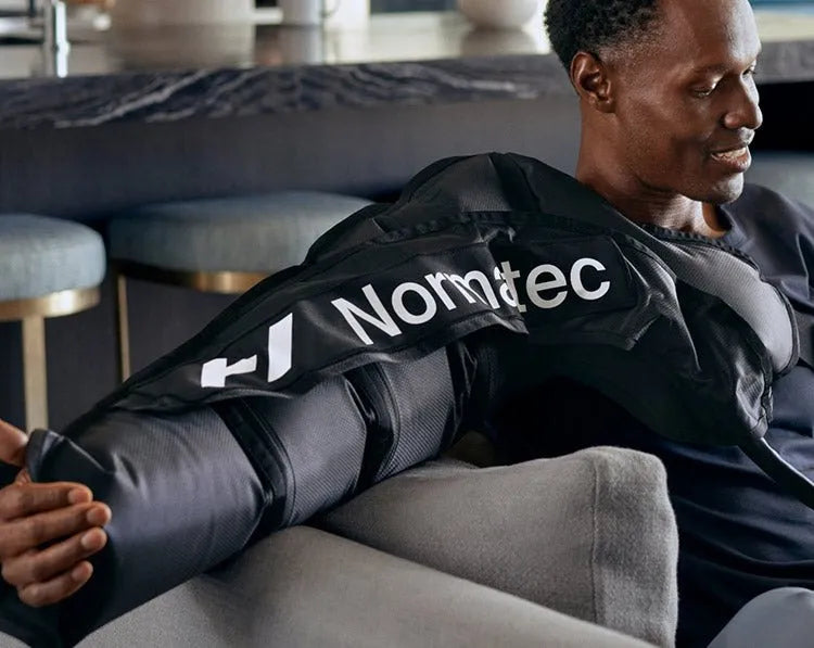 Hyperice Normatec Arm Attachments - A man wearing arm attachment while sitting on a grey sofa