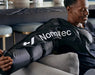 Hyperice Normatec Arm Attachments - A man wearing arm attachment while sitting on a grey sofa