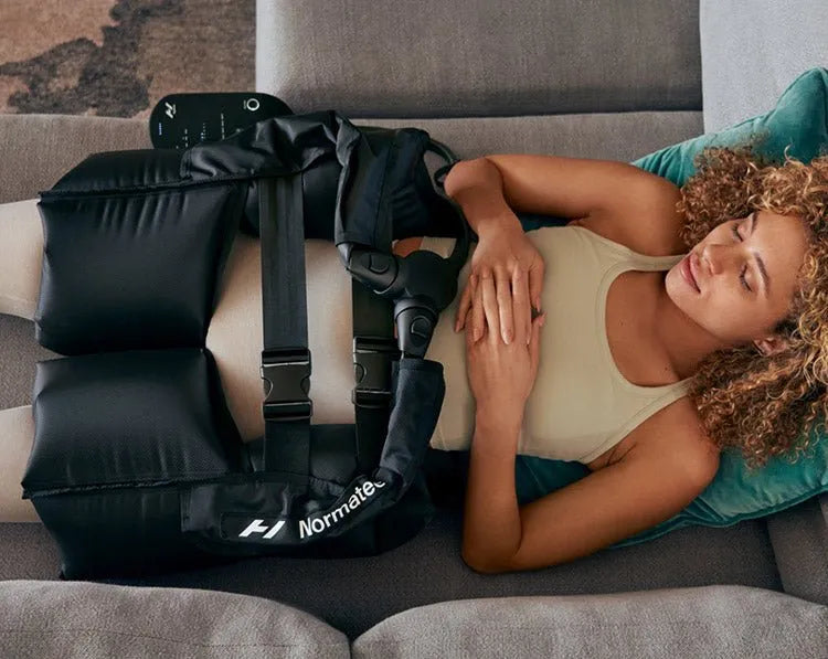 Hyperice Normatec Hip Attachments - Woman laying on a grey sofa with Normatec Hip Attachment