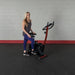 Best Fitness BFUB1 Upright Bike - woman standing in front of the actual product with right foot on the pedal